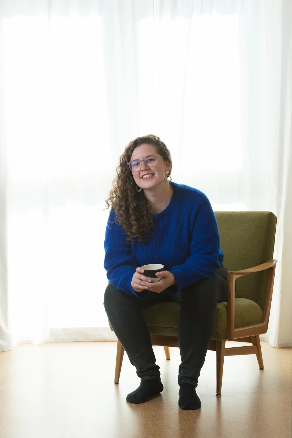 Dorothea Singer sitzt im grünen Sessel in ihrer Praxis Soma & Raum Stuttgart und hält eine Teetasse
